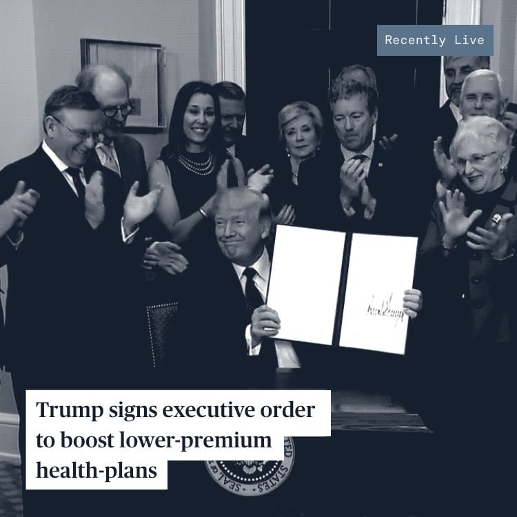 President Trump shows his signature on an executive order while a group of politicians clap behind him.